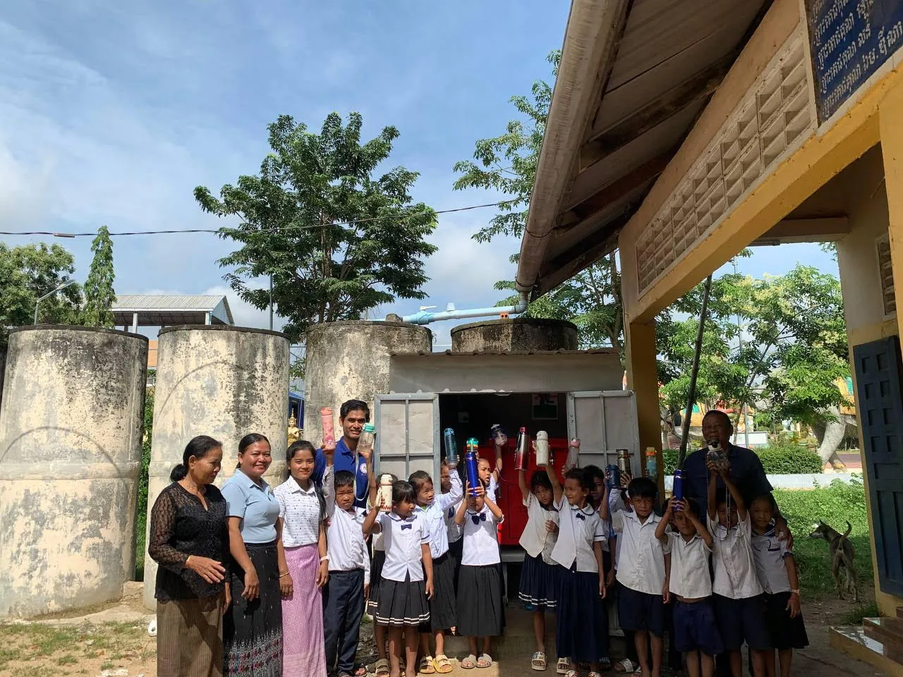 Students and teachers holding up water bottles beside the school water treatment station in Cambodia