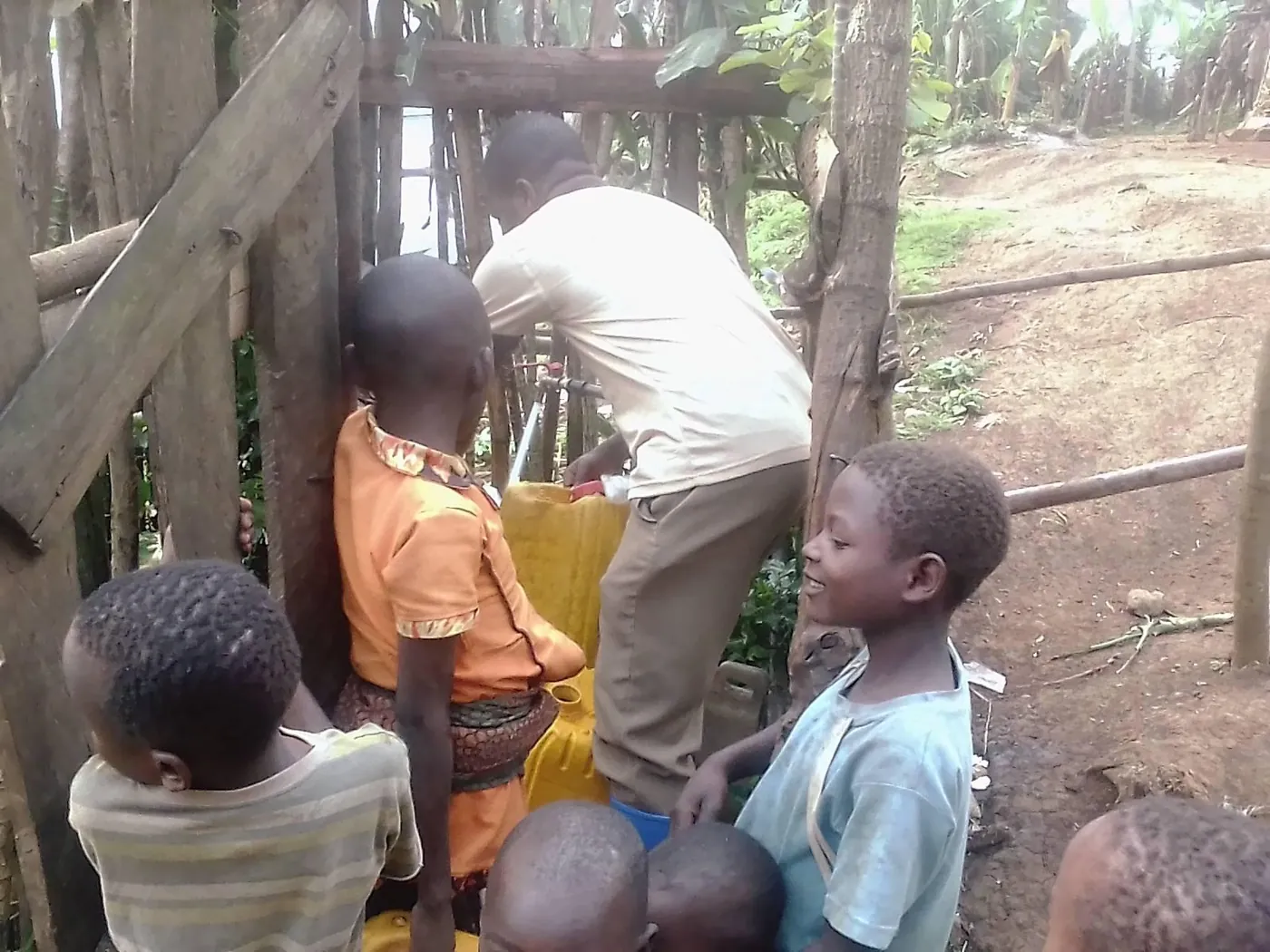 Children and a volunteer filling yellow jerrycans at a community water point in DR Congo